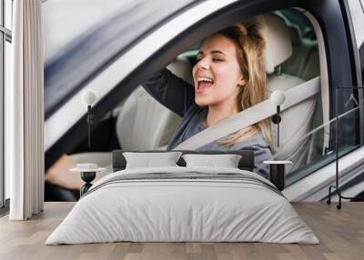 Cheerful young woman driver sitting in car, driving. Wall mural