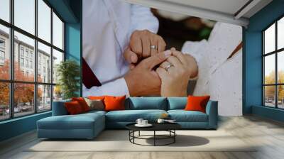 Close-up of bride and groom holding hands with wedding rings at reception outside in the backyard. Wall mural