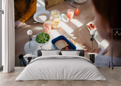 Close-up of mother preparing snack to lunch box in kitchen at home. Wall mural