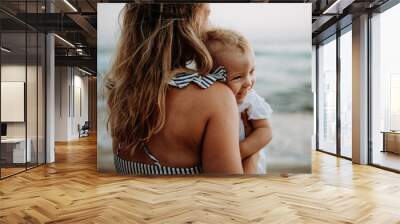 Close-up of young mother with a toddler girl on beach on summer holiday. Wall mural