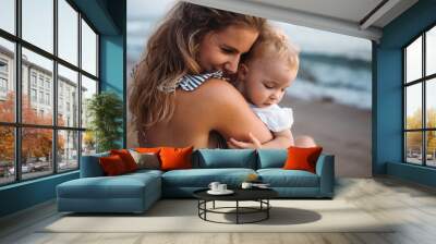 Close-up of young mother with a toddler girl on beach on summer holiday. Wall mural