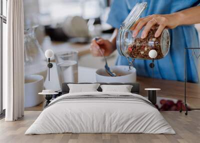 Close-up of young woman preparing muesli for breakfast in her kitchen, morning routine and healthy lifestyle concept. Wall mural