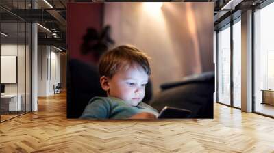 Cute boy sitting on bed watching something on smartphone. Children's screen time. Wall mural