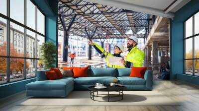 Engineers standing outdoors on construction site, holding tablet. Wall mural