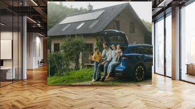 Family with electric car standing in front their house with solar panels on roof. Solar energy and sustainable lifestyle of young family. Concept of green energy and sustainable future for next Wall mural