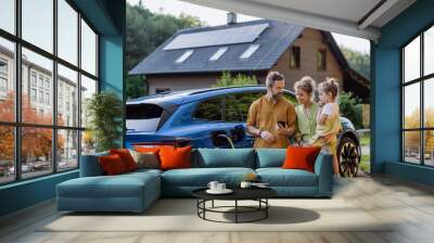 Family with little girl standing in front of their house with solar panels on the roof, having electric car. Wall mural