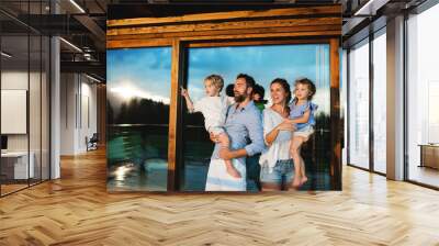 Family with small children standing by wooden cabin, holiday in nature concept. Wall mural