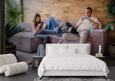 Family with two little daughters, everyone is using mobile phone in the living room. Wall mural