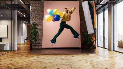 Fashion studio portrait of a happy young woman with balloons jumping, backstage of photoshooting . Wall mural