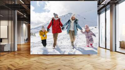 Father and mother with two small children in winter nature, walking in the snow. Wall mural