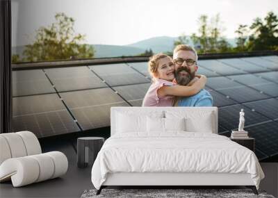 Father with girl on roof with solar panels, hugging, looking at camera. Rooftop solar or photovoltaic system. Sustainable future for next generation. Wall mural