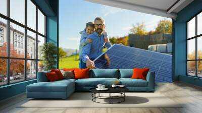 Father with his little daughter catching sun at solar panel,charging at their backyard. Alternative energy, saving resources and sustainable lifestyle concept. Wall mural