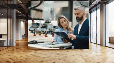 Female engineer and male production manager standing in modern industrial factory, talking about production. Manufacturing facility with robotics and automation. Wall mural