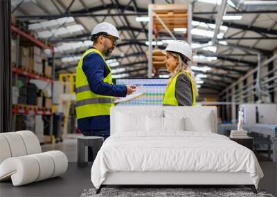 Female engineer and male project manager standing in modern industrial factory by computer, talking about production. Team management in manufacturing facility Wall mural