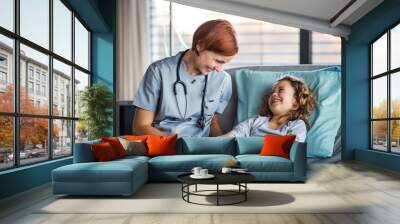 Friendly female doctor examining small girl in bed in hospital. Wall mural