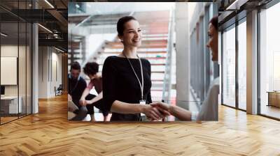 Group of young businesspeople standing on a staircase, shaking hands. Wall mural