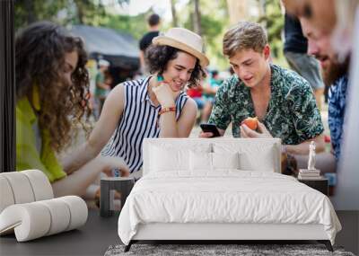 Group of young friends at summer festival, sitting on the ground and eating. Wall mural