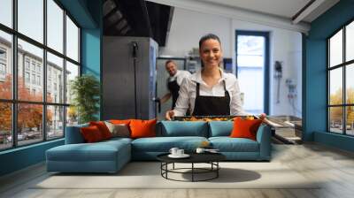 Happy female cook looking at camera and holding tray with baked pumpkin pieces in commercial kitchen Wall mural