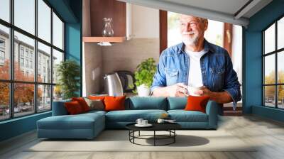 Happy senior man holding a cup of coffee in the kitchen. Wall mural