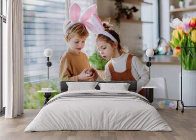 Happy siblings looking at growing plants after decorating easter eggs. Wall mural