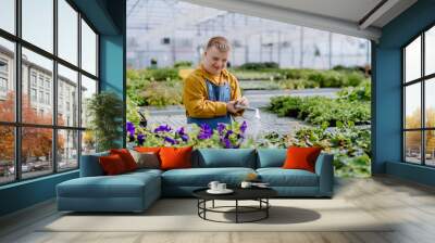 Happy young employee with Down syndrome working in garden centre, watering plants with a shower head and hose. Wall mural