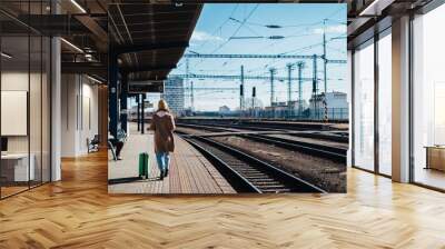 Happy young traveler woman with luggage waiting for train at train station platform Wall mural