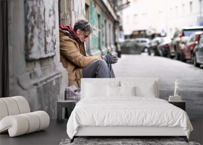 Homeless beggar man sitting outdoors in city asking for money donation. Wall mural