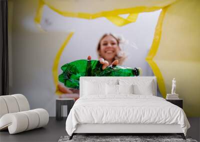 Image from inside yellow recycling bag of woman throwing a plastic bottle to recycle. Wall mural