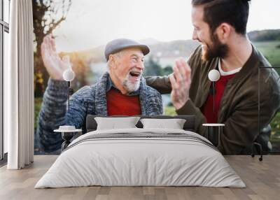 Laughing senior father and his son on walk in nature, giving high five. Wall mural