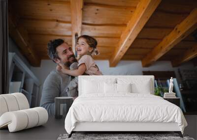 Low angle view of mature father with small daughter having fun indoors at home, holding and hugging. Wall mural