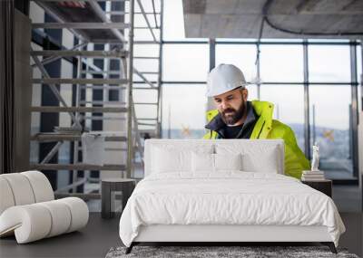 Man engineer standing on construction site, holding blueprints. Wall mural