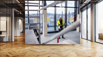 Man engineer standing on construction site, holding blueprints. Wall mural