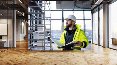 Man engineer standing on construction site, holding blueprints. Wall mural