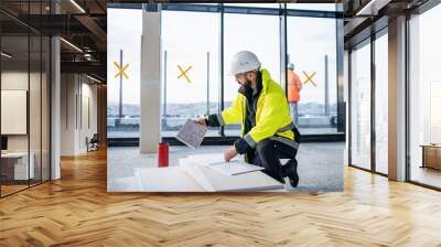 Man engineer with tablet on construction site, looking at blueprints. Wall mural