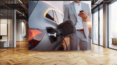 Man holding smartphone while charging car at electric vehicle charging station, closeup. Wall mural