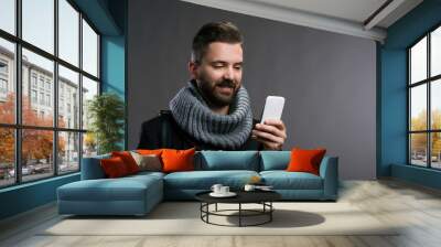 Man in winter clothes with smartphone texting, studio shot Wall mural