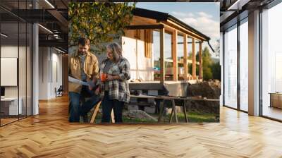 Mature couple having coffee break when working together on construction site of their new house. Wall mural