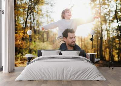 Mature father giving piggyback ride to small daughter on a walk in autumn forest. Wall mural