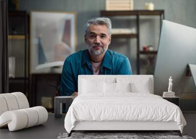 Mature man architect working on tablet at desk indoors in office, looking at camera. Wall mural