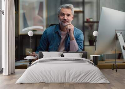 Mature man architect working on tablet at desk indoors in office, looking at camera. Wall mural