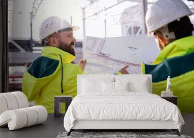 Men engineers standing outdoors on construction site, holding blueprints. Wall mural