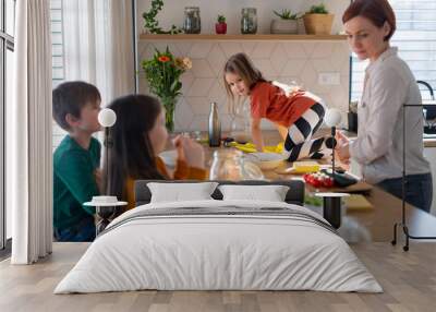 Mother of three little children preparing breakfast in kitchen at home. Wall mural