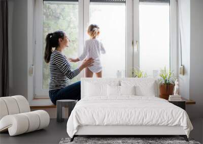 Mother with her little daughter looking out of window Wall mural