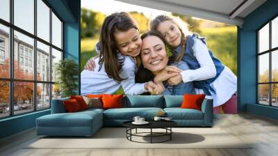 Mother with two small daughters having fun outdoors in spring nature, hugging. Wall mural