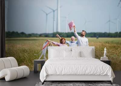 Multigeneration family standing on field on wind farm, playing with kite. Wall mural