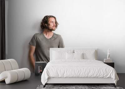 Portrait of a joyful young man with long wavy hair in a studio, hands in pockets. Wall mural