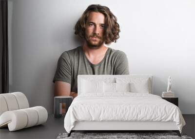 Portrait of a joyful young man with long wavy hair in a studio arms crossed. Wall mural