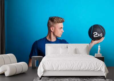 Portrait of a young man holding a heavy ball in one hand in a studio. Wall mural