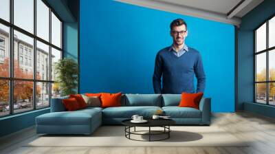 Portrait of a young man with glasses in a studio on a blue background. Wall mural