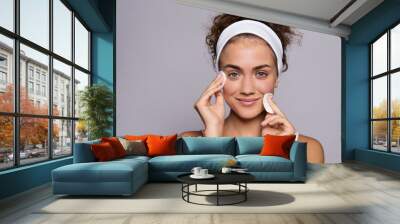 Portrait of a young woman cleaning face in a studio, beauty and skin care. Wall mural